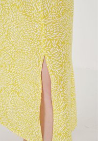 Gul blommönstrad klänning med en sidssnittsdetalj, tillverkad av lätt tyg med en mjuk textur och vita lövdesigns.
