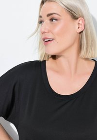 Černé tričko s krátkým rukávem a kulatým výstřihem, vyrobené z texturované tkaniny a volného střihu. Výstřih je doplněn hladkým lemem.