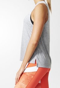 Harmaa ilmanhiha t-paita, jossa on rento leikkaus, sivuhalkiot ja pyöristetty helma, yhdistettynä oransseihin kuviollisiin legginsseihin.