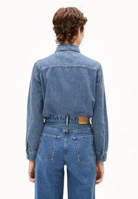 Denim jack in lichtblauw met een kraag, figuurvormig ontwerp en knopenmanchetten. Gepaard met hoge taille jeans voorzien van twee achterzakken.