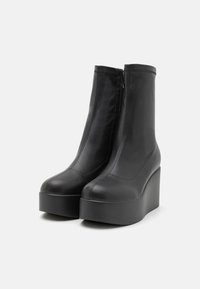 Schwarze Leder-Plateau-Stiefeletten mit glatter Oberfläche, runder Zehenpartie und einem seitlichen Reißverschluss. Erhöhte Keilsohle sorgt für Höhe, ohne voluminös zu wirken.