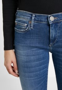 Jeans in denim blu scuro con vestibilità slim, caratterizzati da una vita media, tasche frontali e dettagli di cucitura in evidenza.