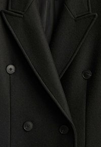 Manteau noir croisé avec de larges revers et quatre boutons noirs, fabriqué en tissu de laine texturé.