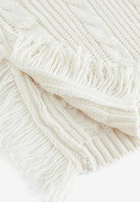 Batikdecke in Off-White mit strukturierten Mustern, versehen mit Fransen an den Rändern. Das Material wirkt weich und gemütlich.