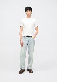 Witte korte mouw T-shirt, lichtblauwe spijkerbroek en donkerbruine schoenen. Losse pasvorm met een gladde textuur. Simpel en casual ontwerp.