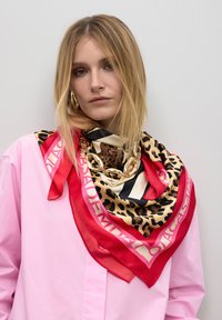 Bufanda de seda con estampado de leopardo, rayas negras y acentos rojos, superpuesta a una camisa rosa, con un detalle de cadena dorada.