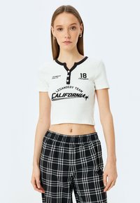 Hvid ribbet crop-top med sorte detaljer, knaplukning og "California" tryk. Sammen med sort-hvide ternede bukser.