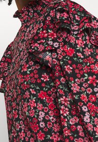 Svart blommig topp med små rosa och röda blommor, smockad halsringning och volangärmar, tillverkad av lättviktsmaterial.