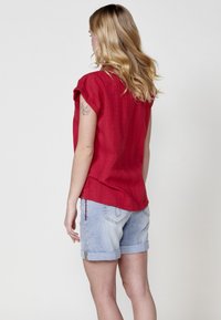 Rode blouse met korte mouwen en gestructureerde strepen, gecombineerd met lichtblauwe denim shorts met opgerolde mouwen en achterzakken.