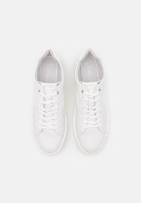 Vita sportskor med ett slätt läderöverdrag, rund tå, platt gummisula och snörning med sex hål. Storlek 42 syns på insidan.