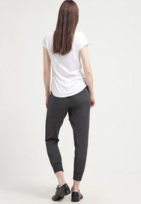 Šedé tepláky vyrobené z měkkého materiálu s manžetami na kotnících, zkombinované s jednoduchým bílým tričkem. Model je otočen zády k fotoaparátu.