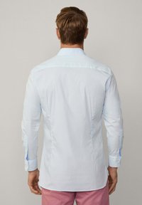 Camisa de rayas azul claro con mangas largas, puños con botones y un corte ajustado. Tela fresca con elementos de diseño minimalistas y yugo trasero.