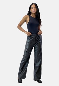 Svart bodysuit med ärmlös design, parade med högmidjade, lös passform av svarta faux läder cargo-byxor med sidofickor.