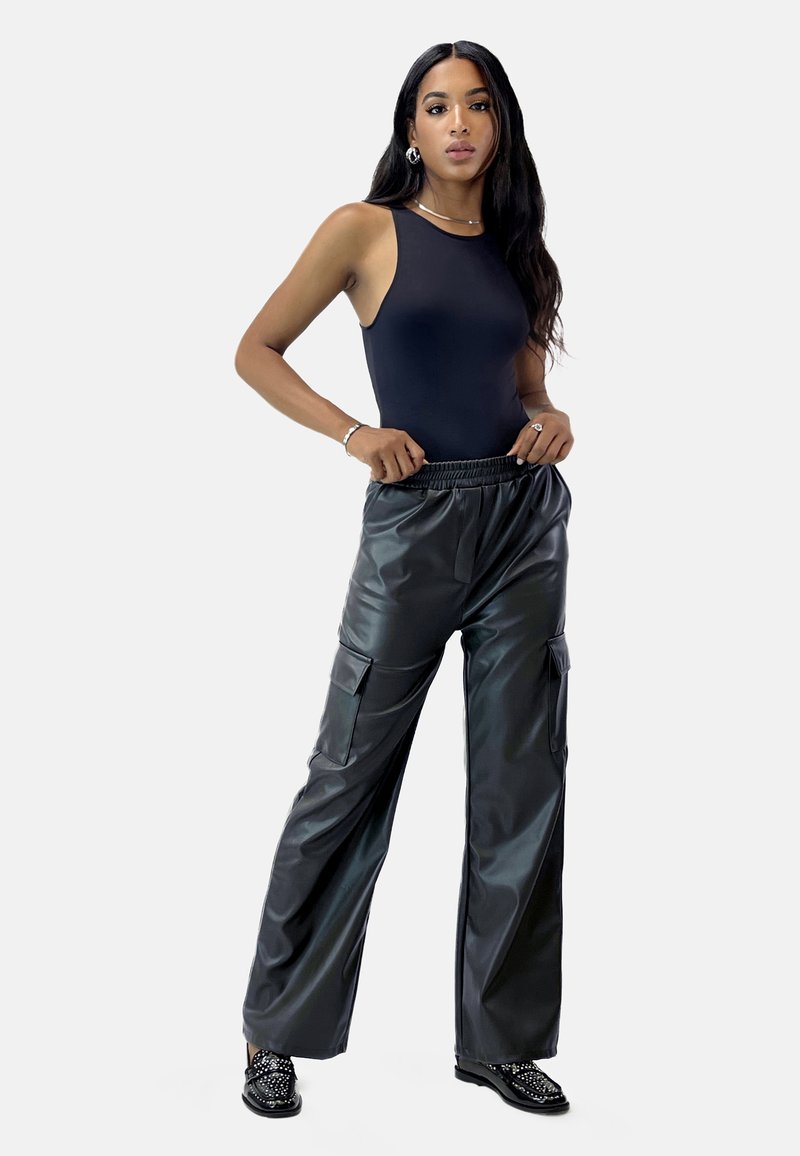 Sort bodysuit med ærmeløs design, parret med højtaljede, løstsiddende bukser i sort kunstlæder med sidelommer.