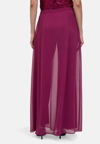 Jupe longue et transparente de couleur bordeaux profond avec un design en A. Elle présente une taille lisse et est doublée pour une silhouette fluide.