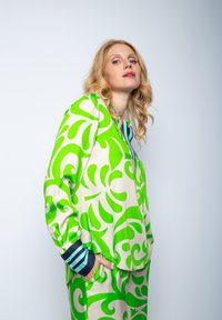 Bluzka w zielono-kremowy wzór z wirującymi wzorami, z długimi rękawami i niebieskim, pasiastym kołnierzem. Wykonana z miękkiego materiału z luźnym krojem.