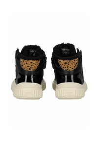 Zapatillas de charol negro con un acento de manchas marrones, cuello de felpa negra y suela de goma beige. Presenta una correa de Velcro para el cierre.