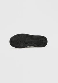 Talpă de pantof din cauciuc negru, cu un model texturat în zigzag, accente circulare de design și o zonă puțin ridicată a călcâiului.