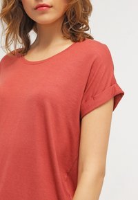 T-shirt rose à coupe décontractée, col rond et manches courtes retroussées, fabriqué à partir d'un tissu doux et léger, présentant une texture lisse.