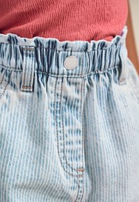 Šviesiai mėlyni džinsiniai šortai, turintys ribotą, elastingą juosmenį, priekinės kišenės ir subtilų vertikalių dryžių raštą. Matomas sidabrinis mygtuko detalė.