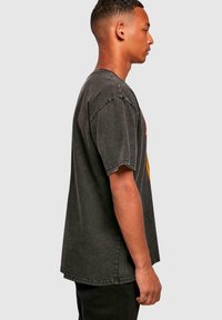 Tmavě šedé oversized tričko s kulatým výstřihem a krátkými rukávy. Na přední straně má barevnou grafiku a roztrhané okraje.