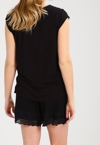 Haut noir à manches courtes en tissu doux, associé à un short noir avec une bordure en dentelle le long de l'ourlet.