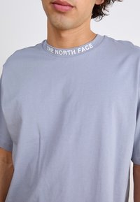 Šviesiai mėlynas medvilninis marškinėliai su trumpomis rankovėmis ir apvaliu kaklu. Balta "The North Face" logotipas aplink kaklo liniją. Lygaus paviršiaus, kasdienio dizaino.