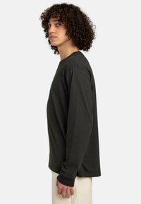 Schwarzes langärmliges T-Shirt aus Baumwolle. Verfügt über einen Rundhalsausschnitt und schmal geschnittene Bündchen. Seitenansicht, die einen entspannten Schnitt und ein einfaches Design hervorhebt.