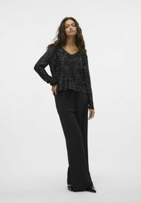 Top nero a maniche lunghe con scollatura a V e motivo testurizzato, abbinato a pantaloni neri larghi, che offre una silhouette e una vestibilità rilassate.