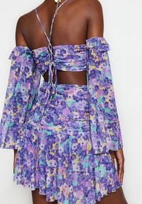 Lilla blomsterprintet to-delt sæt med ærmer, der sidder uden på skuldrene, flæsekant og tætsiddende design med bindebånd bagpå.