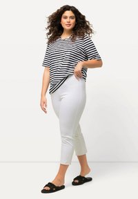 Camicia a maniche corte a V a righe bianche e nere abbinata a pantaloni bianchi alla caviglia e sandali neri con texture.