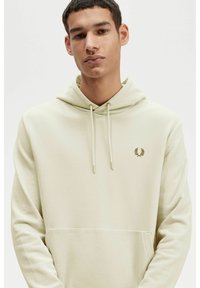 Sudadera color beige claro, tela de algodón, bolsillo tipo canguro, capucha ajustable con cordón, logotipo dorado en el pecho, textura suave, corte relajado.