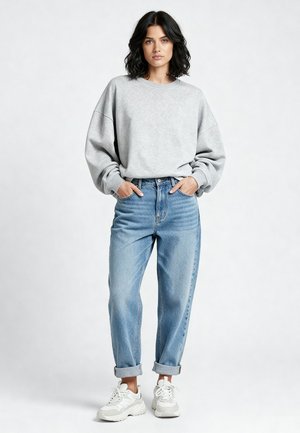 Felpa grigia con spalle scese, jeans blu a vita alta e sneakers bianche con suola texture; outfit casual su sfondo neutro.