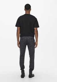 Zwarte t-shirt met korte mouwen, gecombineerd met donkere, gestreepte broek. De broek heeft een vierkant patroon en een slim fit, afgemaakt met zwarte laarzen.