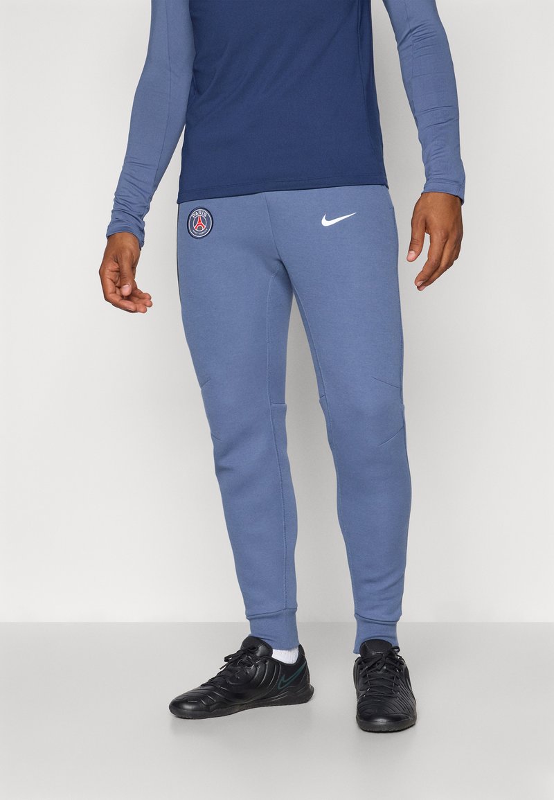 Nike joggers i lyseblåt stof med tætsiddende ben, der viser et Paris Saint-Germain-logo på venstre lår og en hvid Nike swoosh.