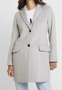 Light gray wool coat, tailored design, single-button closure, notched lapels, two front pockets, smooth texture. Worn over a gray hoodie.