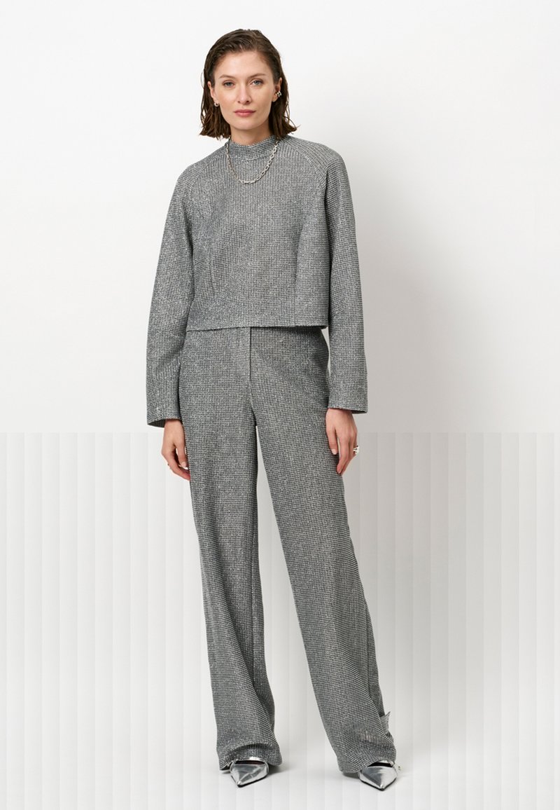 Grijze textuur cropped sweater met lange mouwen, gecombineerd met hoge taille wijde broek, beide met een houndstoothpatroon. Zilveren accessoires.