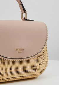Wiklinowa torebka ze słomy z kremową górą i teksturowaną różową klapką. Złote okucia i czarny akcent wzdłuż krawędzi klapki.