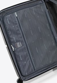 Intérieur d'une valise spinner avec un tissu sombre à motif rayé, une poche zippée en maille et une étiquette de marque. Compartiments de rangement visibles.