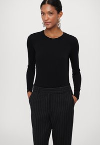 Bodysuit noir à manches longues associé à un pantalon à rayures sombres. La tenue présente une silhouette ajustée et une texture de tissu lisse.
