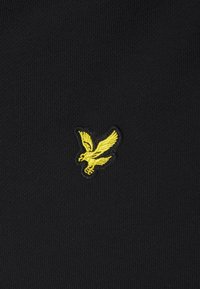 Oiseau jaune brodé avec les ailes déployées sur un fond en tissu noir texturé.