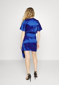 Robe en satin bleu à manches courtes et au design croisé, avec un motif subtil de imprimé animal. Associée à des chaussures à talons hauts noires.