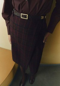 Plaid wool skirt in dark burgundy with green accents, featuring a high-waisted design and a black belt with a gold buckle.