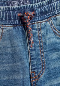 Șorturi din denim cu o nuanță albastră, prezentând un tiv elastic și un șnur albastru închis cu accente portocalii. Detaliu distinctiv de cusătură.