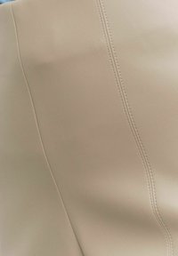 Beige kunstleer materiaal met een gladde textuur, met een opvallende naad die het oppervlak accentueert. Eenvoudige, moderne ontwerpdetails zijn zichtbaar.