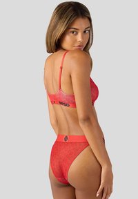 Rood leopardenprint lingerie set gemaakt van zachte stof. Beschikt over verstelbare bandjes en een elastische tailleband met logo-detail. Achteraanzicht.