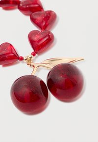 Red resin cherry earrings with a gold metal leaf detail, complemented by red heart-shaped beads and small red spherical accents.
