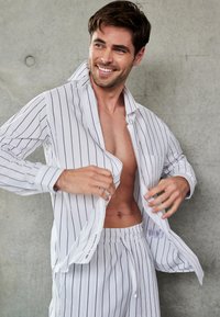Hvide stribede pyjamas bestående af en knappet skjorte og shorts med elastisk talje. Glat stof med en afslappet pasform og justerbart snoretræk.