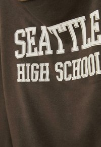 T-shirt in cotone marrone con lettere bianche in stile blocco che leggono "SEATTLE HIGH SCHOOL", con una trama liscia e una vestibilità comoda.