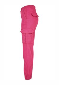 Pantalon cargo rose avec poches à rabat latérales, poignets élastiques et passants de ceinture, présenté de profil sur fond blanc.